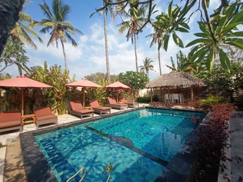 a pool with chairs and umbrellas and palm trees at Villa Kinagu in Gili Meno