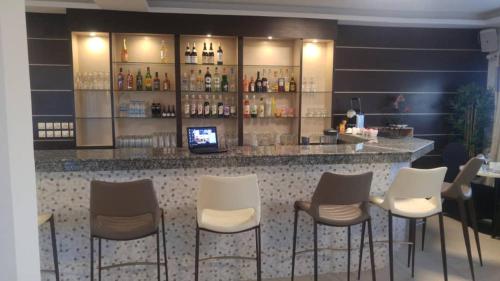 a bar with white chairs and a counter with liquor bottles at Lorenzo Hôtel Abidjan in Abidjan