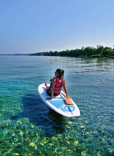 a girl sitting on a surfboard in the water at VVF Lac Léman Évian-les-Bains in Évian-les-Bains