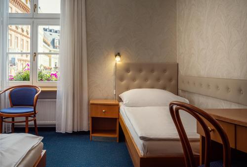 カルロヴィ・ヴァリにあるHotel Ruzeのベッド、デスク、窓が備わるホテルルームです。