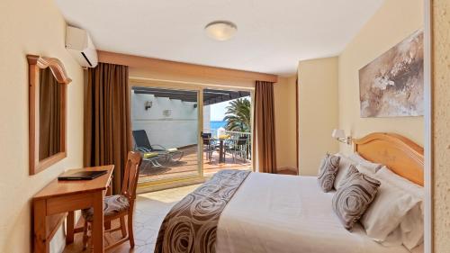 a bedroom with a bed and a desk and a balcony at Macdonald Leila Playa Resort in La Cala de Mijas