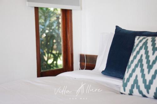 a white bed with a blue pillow and a window at Villa Allure Koh Mak in Ko Mak