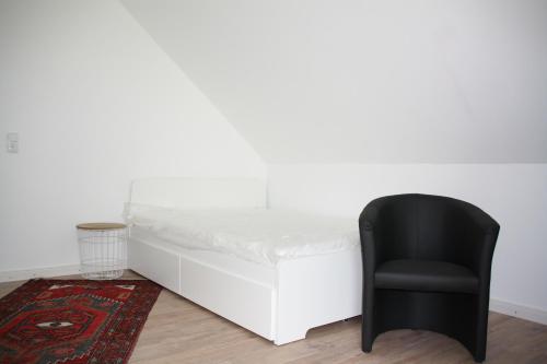 uma cadeira preta sentada ao lado de uma cama branca em Apartment Schoene Aussicht em Langwedel