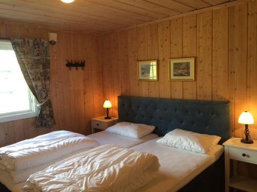 two beds in a bedroom with wooden walls and two lamps at Kjøniksbu - 3 bedroom cabin in Ål