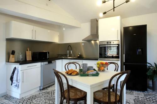 une cuisine avec une table blanche avec des chaises et un réfrigérateur noir dans l'établissement Les Gîtes de Laure - L'Or Vert, Appartement avec Vue sur le Château, Parking Privé, Climatisation, Netflix, à 160 m de la Cité Médiévale, à Carcassonne