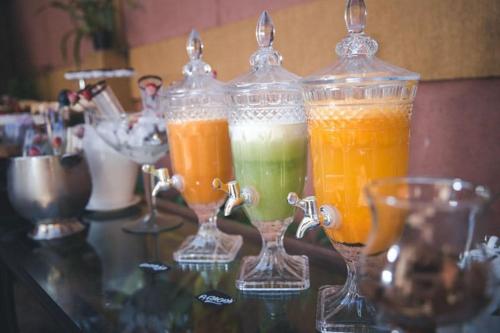 four glass containers filled with different colored drinks on a table at Café Palace Hotel in Três Pontas