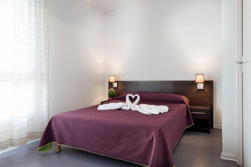 a bed with a purple bedspread with a white ribbon at Residhotel Les Hauts d'Andilly in Andilly