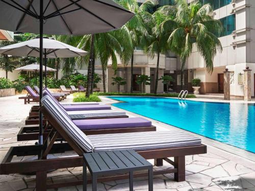 a pool with lounge chairs and umbrellas next to a hotel at Pullman Kuala Lumpur City Centre Hotel & Residences in Kuala Lumpur