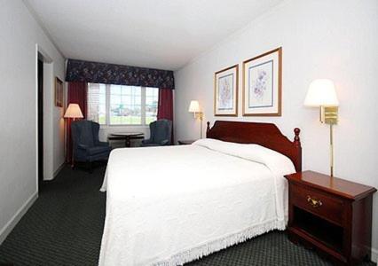 Habitación de hotel con cama blanca y silla en Ambassador Inn, en Fayetteville