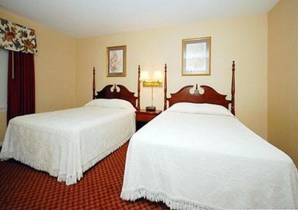 two beds in a hotel room with white sheets at Ambassador Inn in Fayetteville