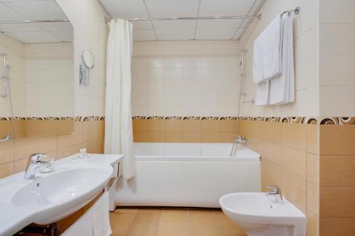 een badkamer met 2 wastafels, een bad en een toilet bij Maxima Panorama Hotel in Moskou