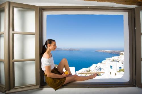 a woman sitting on a window sill looking out at the ocean at Sophia Luxury Suites in Imerovigli