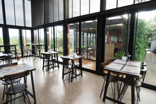 a restaurant with tables and chairs and large windows at Hug Jang Loei Garden & Resort in Ban Na Dan