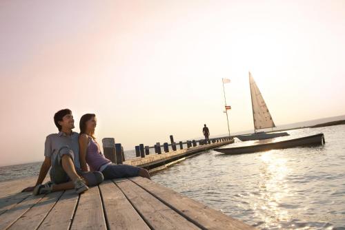 a man and woman sitting on a dock with a sailboat at Das-Schmidt Privathotel in Mörbisch am See