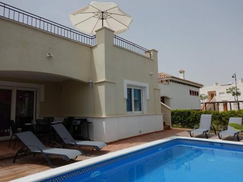 a pool with chairs and an umbrella next to a house at 2-bedroom Villa with pool in Torre-Pacheco