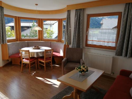 ein Wohnzimmer mit einem Tisch, Stühlen und Fenstern in der Unterkunft Appartements Daisy in Serfaus