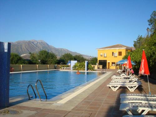 a swimming pool with chairs and umbrellas next to a building at Camping Rural Presa La Viñuela in Viñuela
