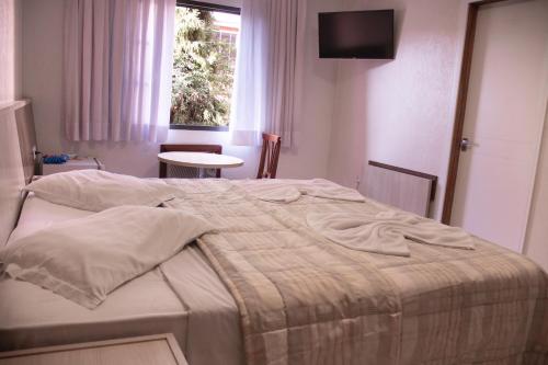a bedroom with a bed and a window and a table at Hotel Colonia in Araucária