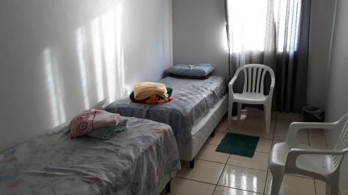 two beds in a small room with a chair and a table at Edifício Belio in Cascavel