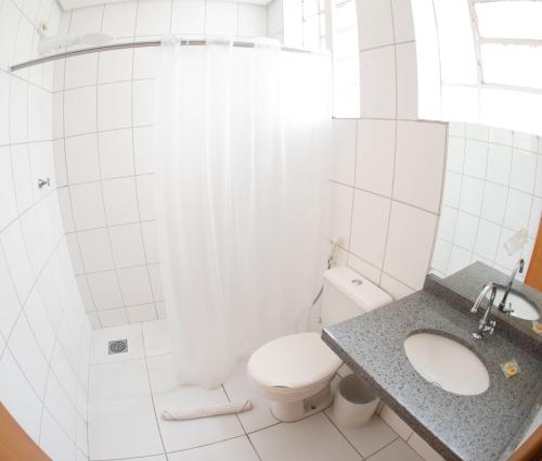 a white bathroom with a toilet and a sink at Getúllio Hotel in Cuiabá