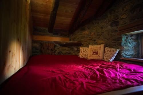 Una cama roja en una habitación con una pared de piedra. en Redelnascht, en Gressoney-la-Trinité