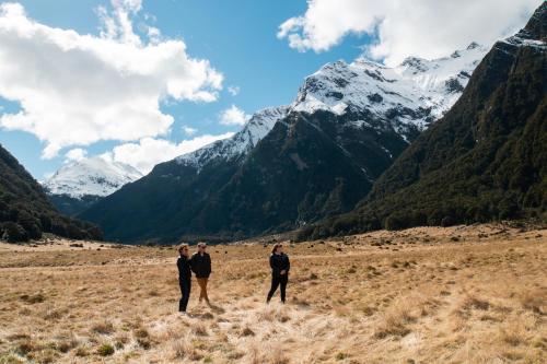 three men standing in a field with mountains in the background at Wonderland Makarora Lodge in Makarora