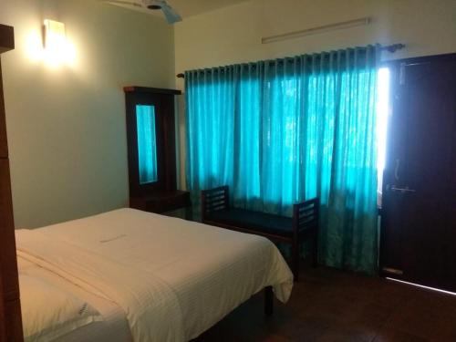 a bedroom with a bed and a window with blue curtains at Shamrock Holiday Home in Munnar