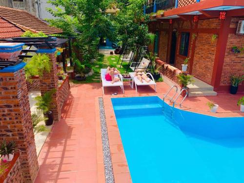a pool with two people sitting in chairs next to a house at Vu's Homestay in Phong Nha