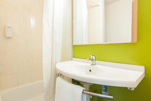 a bathroom with a sink and a mirror and a tub at B&B HOTEL Bordeaux Lac sur Bruges in Bruges