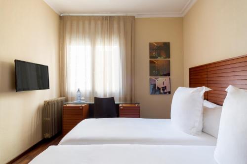 a hotel room with two beds and a desk and a television at Hotel Astoria in Barcelona