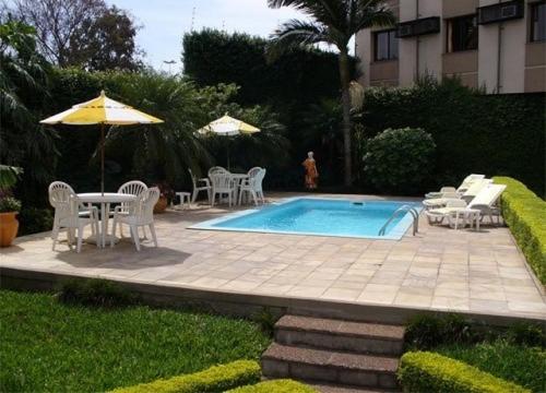 uma piscina com cadeiras e mesas e um guarda-sol em River Hotel em Uruguaiana