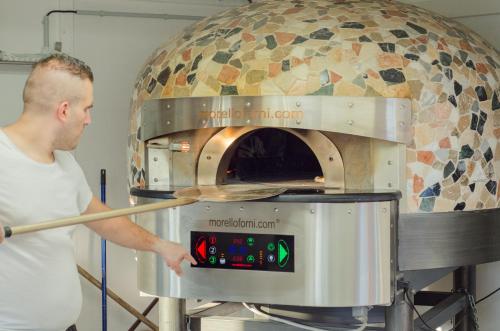 un hombre está poniendo una pizza en un horno en Camping La Bergerie Plage, en Hyères