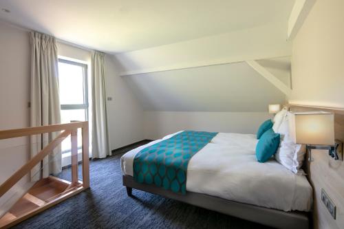 a hotel room with a bed with blue pillows at Best Western Plus Hotel & SPA Le Schoenenbourg in Riquewihr