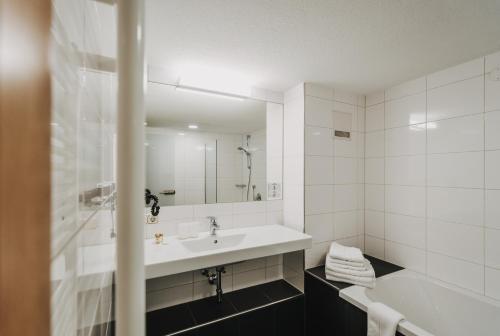 a white bathroom with a sink and a mirror at Hotel Adler in Warth am Arlberg