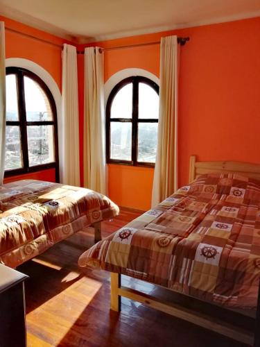 two beds in a room with orange walls and windows at Casa Tréveris in Sucre