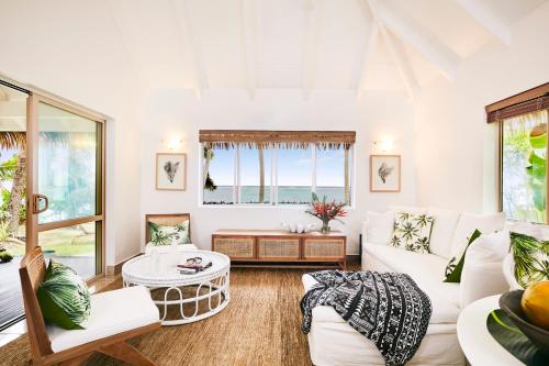 a living room with white furniture and a large window at Motu Beachfront Art Villas in Rarotonga