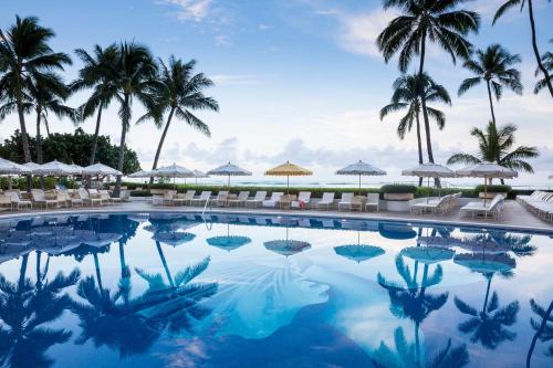 einen Pool mit Palmen und Sonnenschirmen in der Unterkunft Halekulani in Honolulu