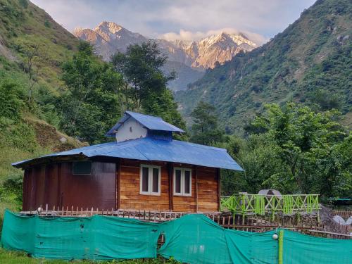 a small house with a blue roof with mountains in the background at The Solitude Camp in Pālampur