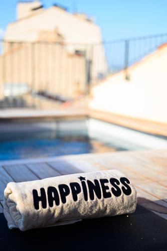 a towel with the word happiness sitting on top of a bed at Grand Hôtel Dauphiné Toulon, Boutique Hôtel & Suites in Toulon