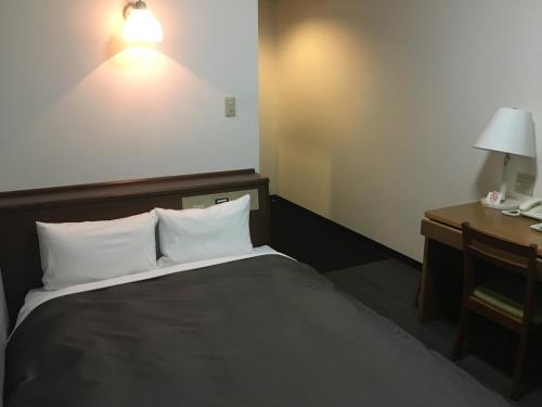 a hotel room with a bed and a desk with a lamp at Garden Hotel Matsumoto in Matsumoto