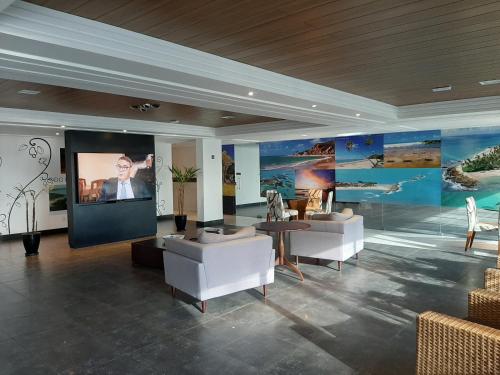 a living room with white furniture and a large screen at Flat Mar do Cabo Branco Residence in João Pessoa