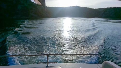 a boat on a body of water with the sun shining at Luxury Apartment with Private Heated Pool in Šibenik