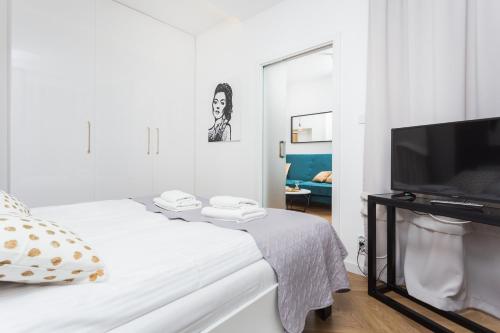 a white bedroom with a bed and a flat screen tv at City of the Kings-Bacalar Apartment in Krakow