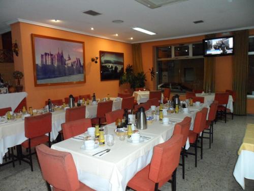 Hostal Coruña في أستورغا: غرفة طعام مع طاولات بيضاء وكراسي حمراء