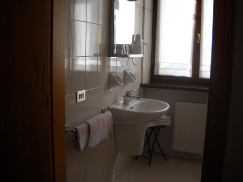 baño blanco con lavabo y ventana en Albergo Chiara, en Alleghe