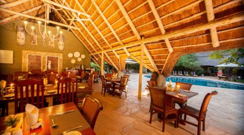 a dining room with tables, chairs, and a pool at Bayete Guest Lodge in Victoria Falls