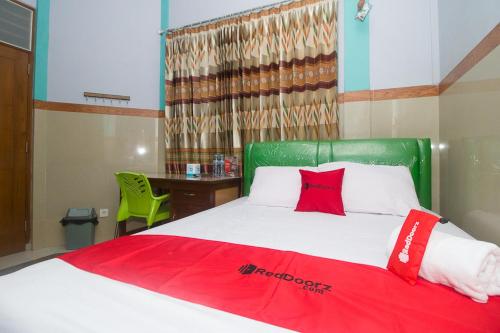 a bedroom with a bed with a green headboard and a desk at RedDoorz Syariah near Alun-Alun Bojonegoro in Bojonegoro