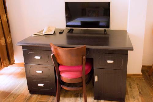 a desk with a television and a chair in a room at Fort Fun City Hotel Fort Portal in Fort Portal