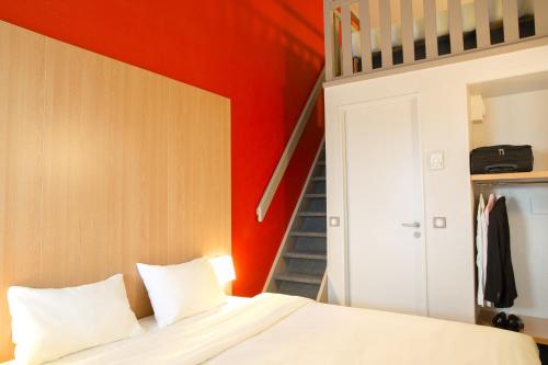 サン・ジャン・ド・ヴェダにあるB&B HOTEL Montpellier 2の赤い壁のベッドルーム1室、白いシーツ付きのベッド1台が備わります。