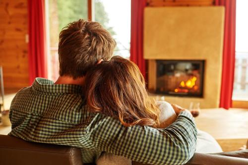 a man and woman sitting on a couch looking at a fireplace at BöckLodges in Nesselwang